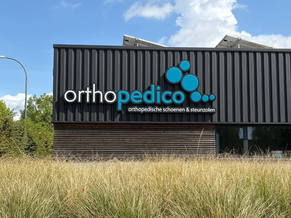 Bedrijfsgebouw Orthopedico in Sint-Truiden met antracietzwart gespoten profielplaatgevel en logo — airless spuitwerken door Fresh Decor