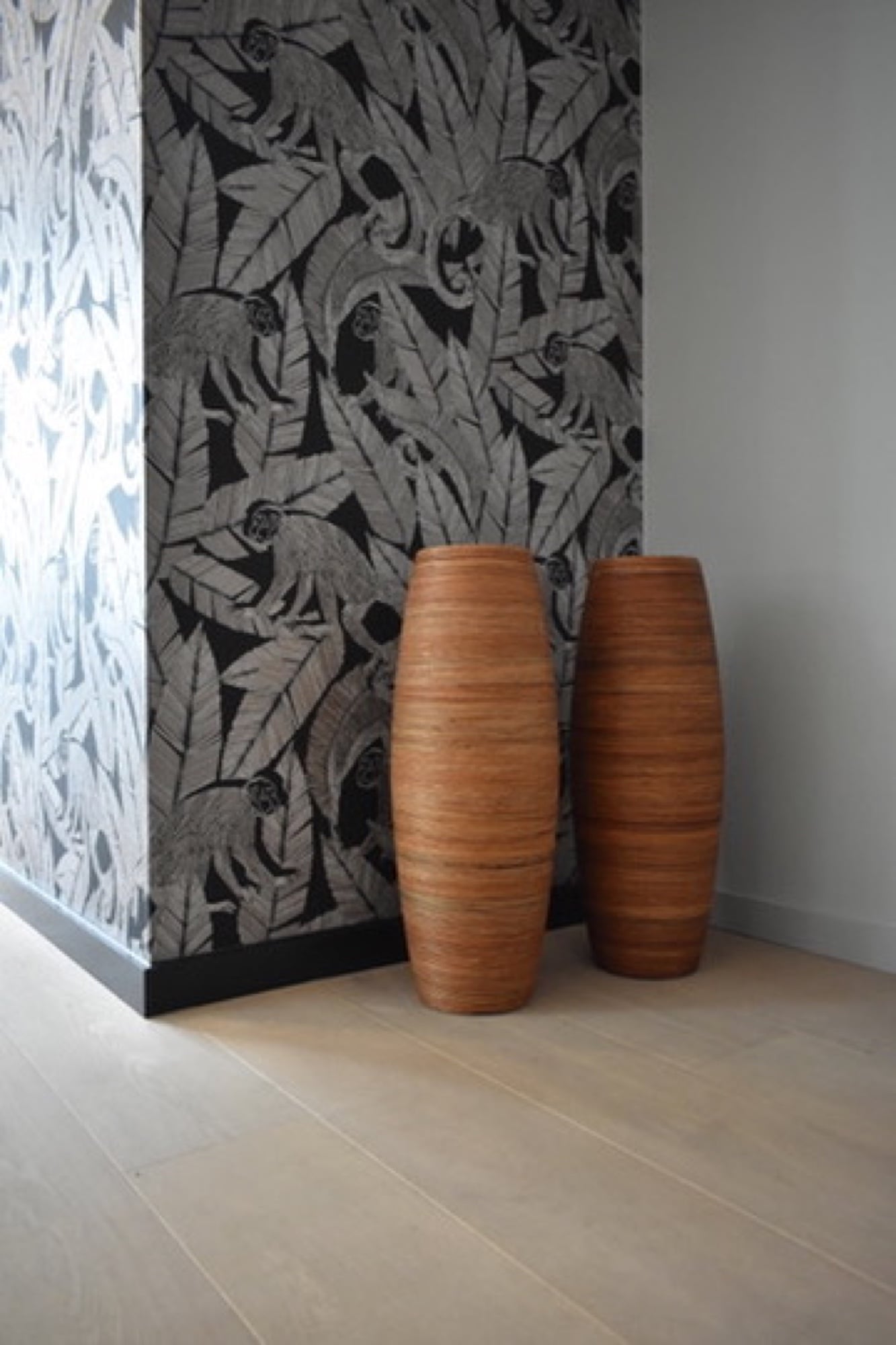 Modern zwart-wit behang met apen en tropische bladeren naast een strak wit vlak, met decoratieve vazen op een houten vloer — behangen door Fresh Decor Limburg