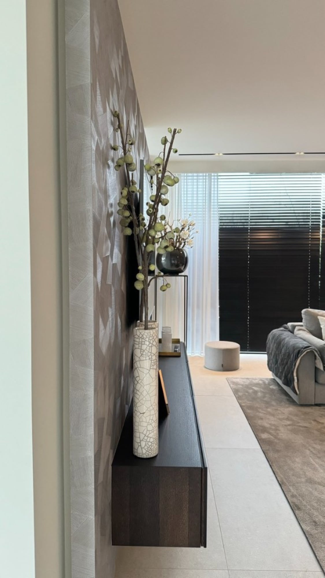 Luxe structuurbehang in zilvergrijs in een moderne hal met zwevend meubel en vazen — behangwerken door Fresh Decor Limburg