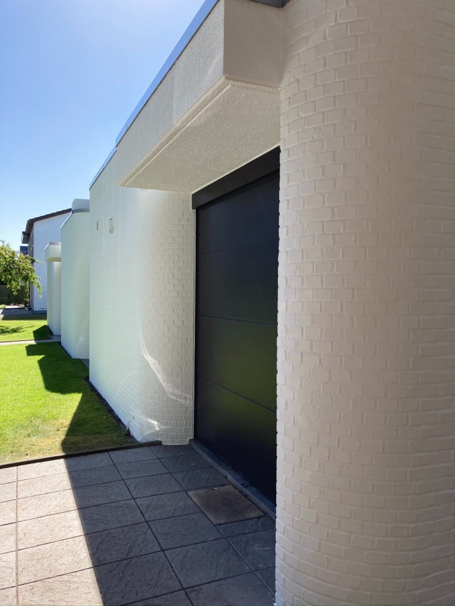 Detail moderne gevel: wit geschilderde bakstenen muur met donkere voordeur en overstek — gevelschilderwerk door Fresh Decor Limburg