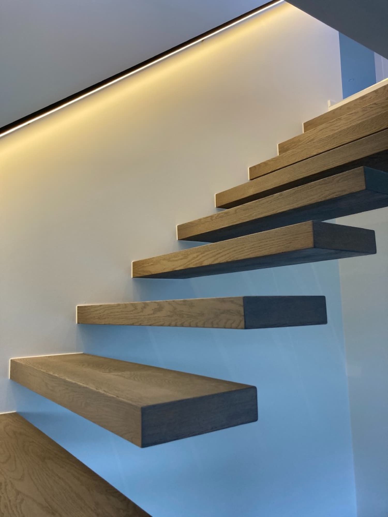 Detailopname van zwevende eiken treden met LED-strip verlichting en strakke witte wand — Fresh Decor Limburg