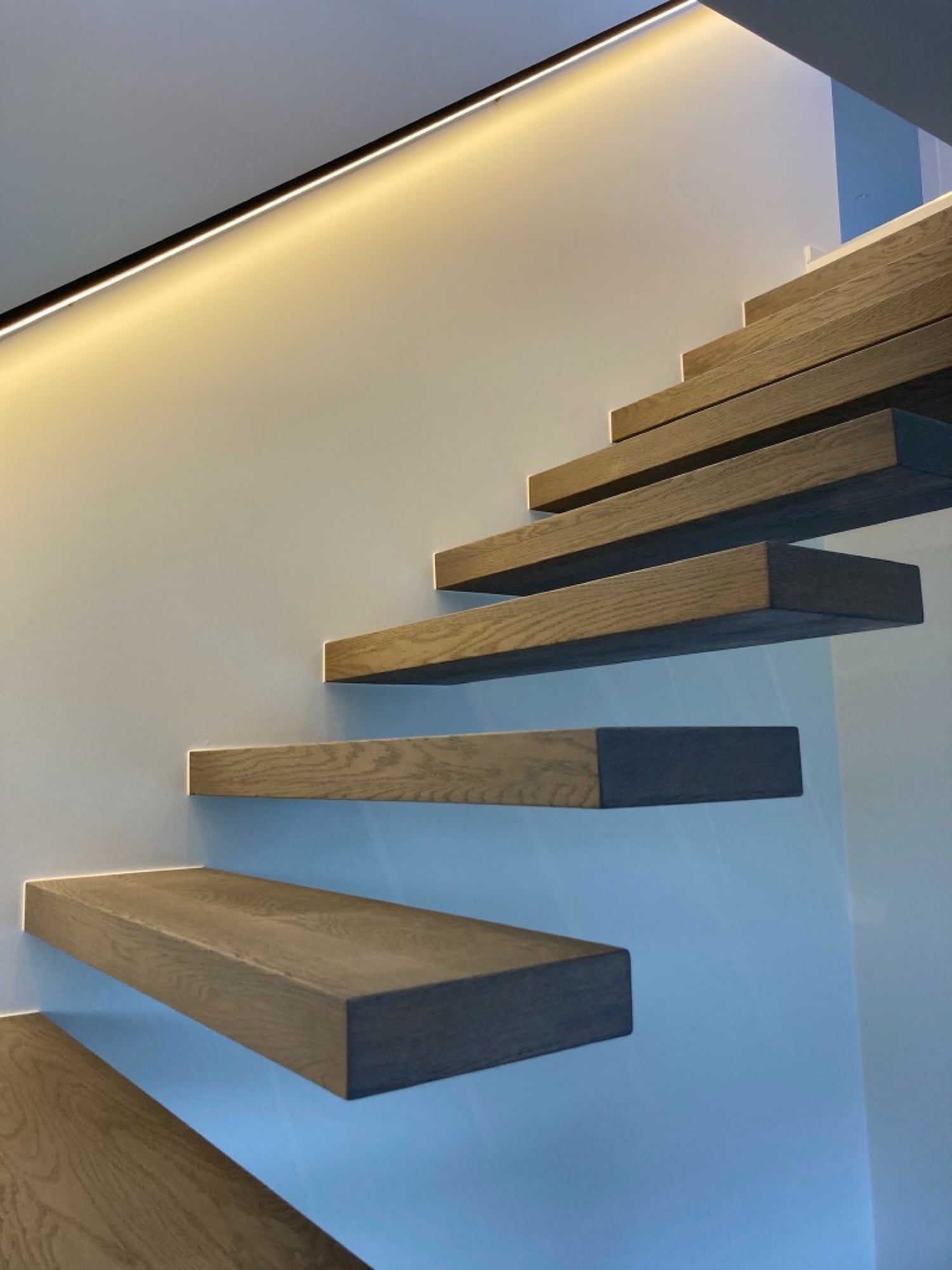 Detailopname van zwevende eiken treden met LED-strip verlichting en strakke witte wand — Fresh Decor Limburg